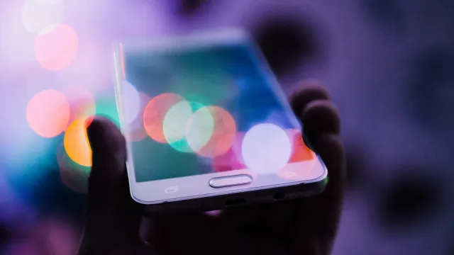 Hand hält ein Smartphone vor bunten Lichtpunkten im Dunkeln – Lovoo Erfahrungen mit der Dating-App