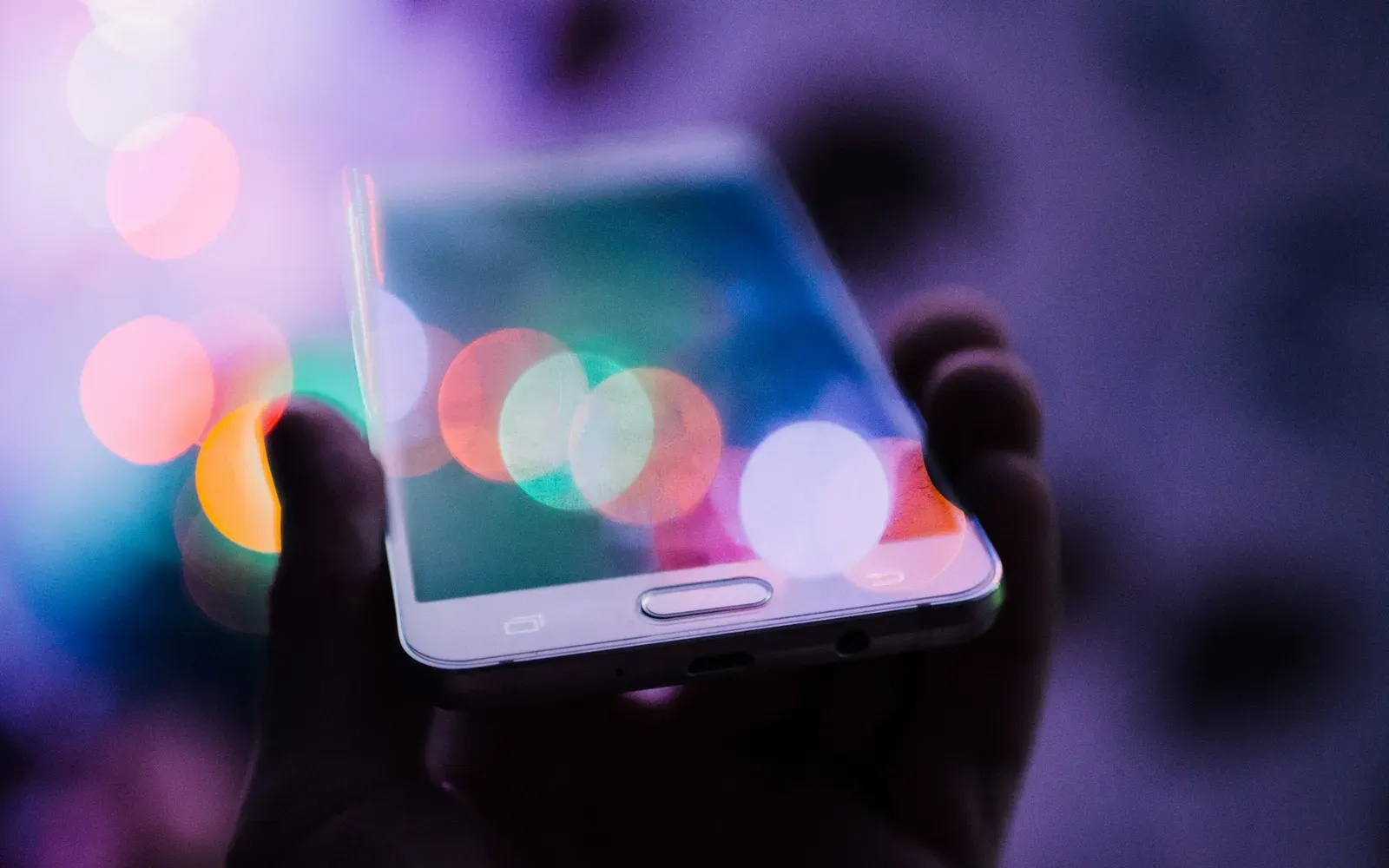 Hand hält ein Smartphone vor bunten Lichtpunkten im Dunkeln – Lovoo Erfahrungen mit der Dating-App