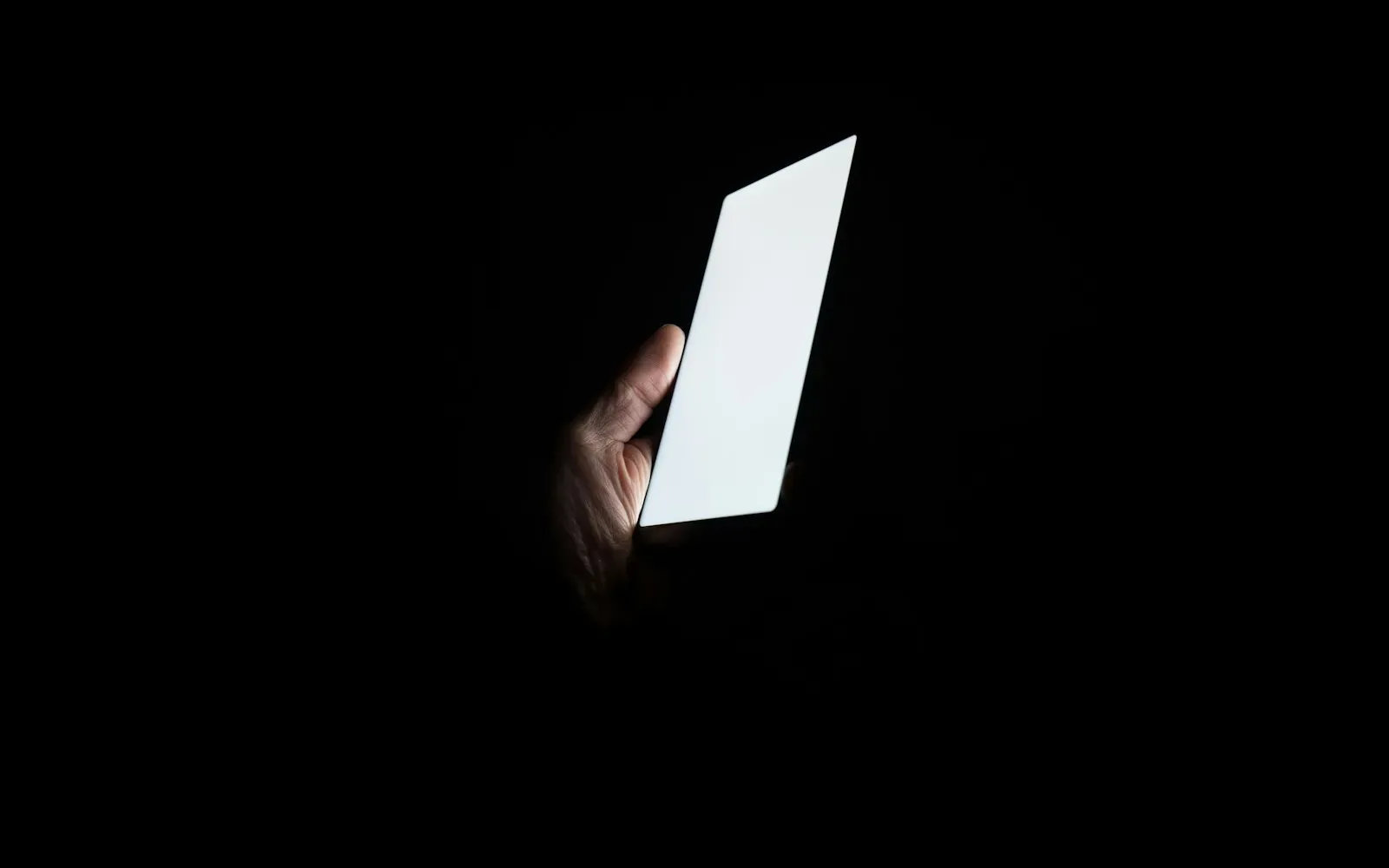Hand hält ein hell leuchtendes Smartphone in völliger Dunkelheit – Poppen.de oder Joyclub im Vergleich