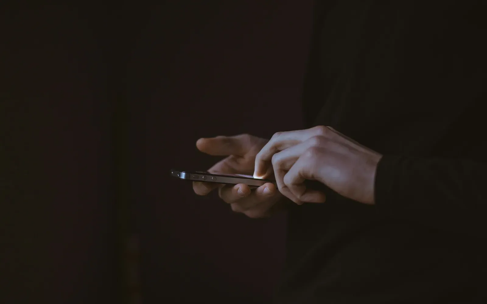 Hände tippen im Halbdunkel auf einem Smartphone